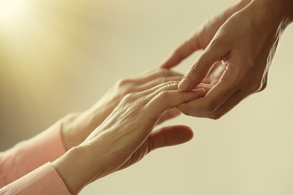 Persona sostiene las manos de una persona mayor